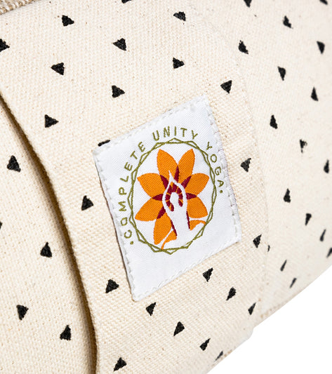 Complete Unity Yoga Zafu Meditation Cushion with a natural print featuring small black triangles. The cushion is designed for yoga and meditation practices, offering comfort and support. The label displays the Complete Unity Yoga logo with an orange and white floral design.