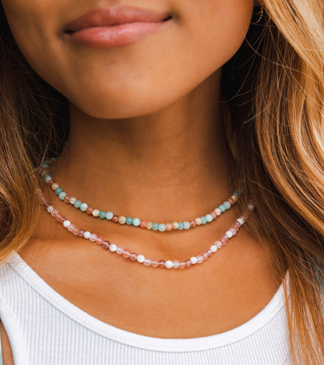 Lotus and Luna Yoga Necklaces featuring Quartz and Mother of Pearl beads are elegantly displayed. These handcrafted necklaces are designed to enhance your yoga practice with their calming and balancing properties. Perfect for those seeking stylish and meaningful yoga accessories.