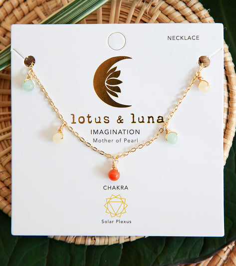 Lotus and Luna's Mother of Pearl Yoga Necklace features a gold chain adorned with colorful beads, designed for enhancing yoga practice. The necklace emphasizes chakra alignment, specifically targeting the solar plexus, and is part of their 